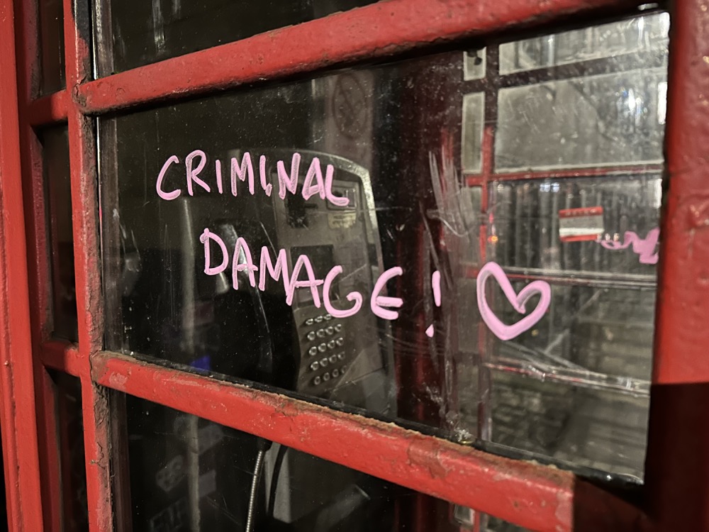 A phonebox with the words criminal damage graffitied on it